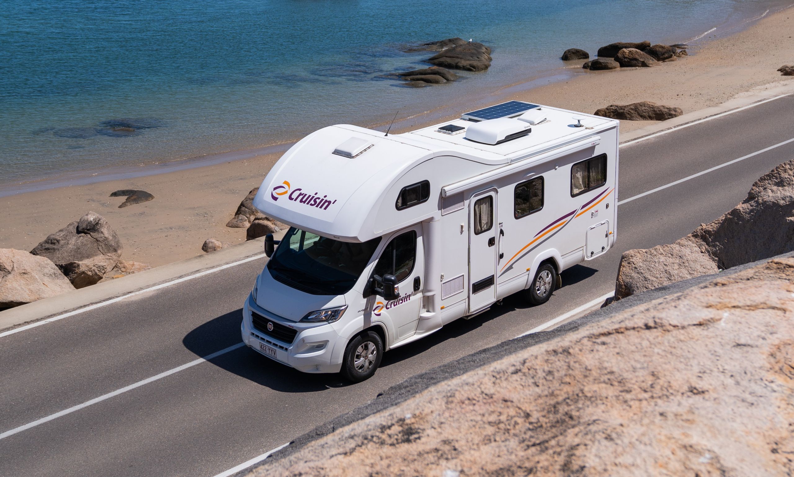 Cruisin' Seeker camper rijdt op een weg langs het strand waar iemand aan het suppen is in zee