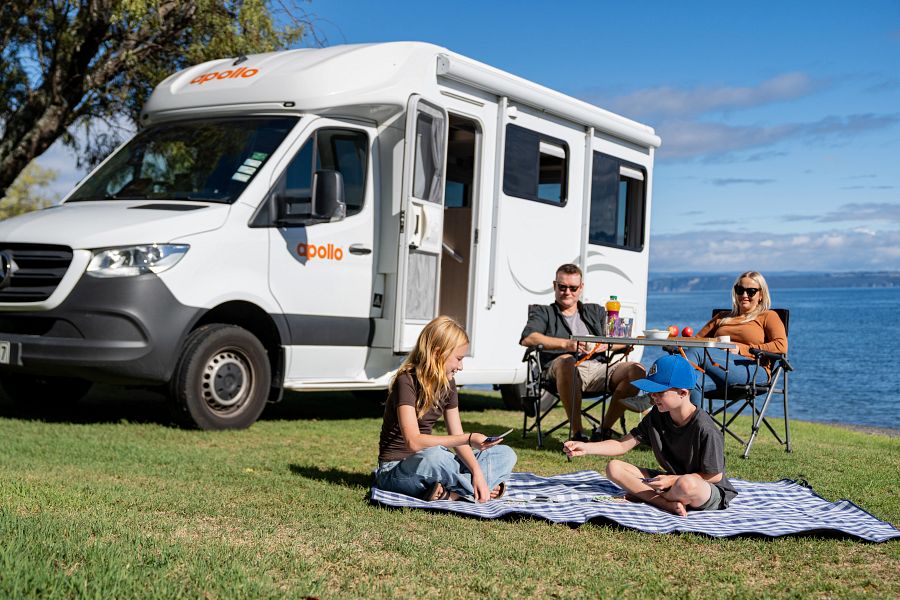 Twee kinderen op een picknickkleed spelen een spelletje, ouders zitten voor de Apollo Euro Quest camper