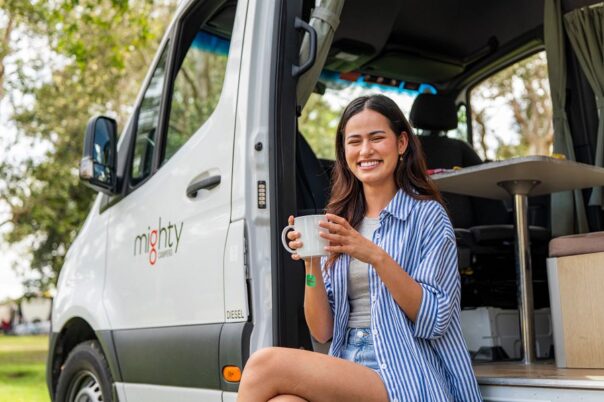 Vrouw geniet van kopje thee in de deuropening van de Mighty Deuce camper