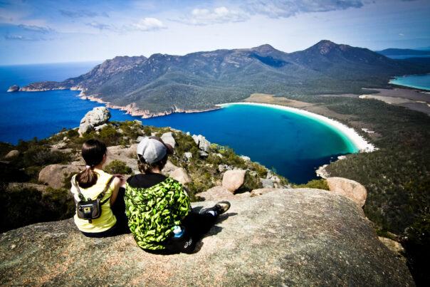 Twee mensen zitten op een rots en kijken uit over Wineglass Bay in Freycinet National Park