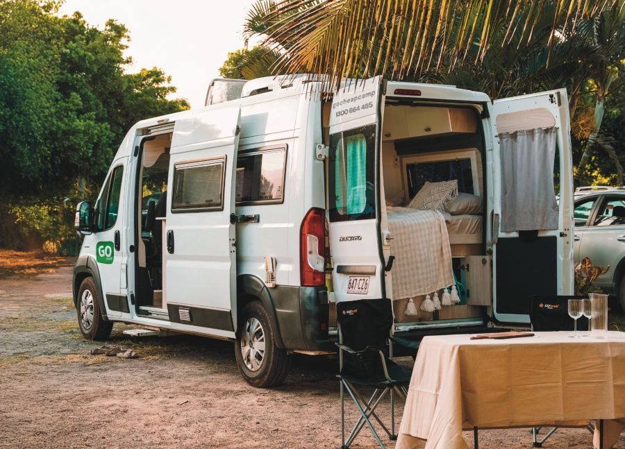 Go Cheap Tamar geparkeerd op een camping met de zij- en achterdeuren open en stoelen met tafel buiten