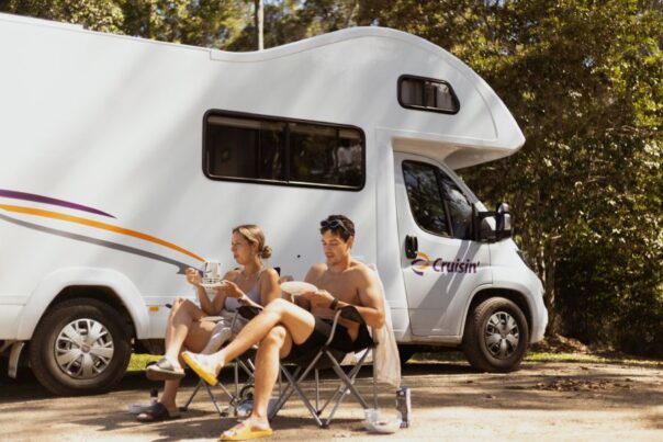 Koppel zit in campingstoelen voor de Cruisin' Seeker camper en is aan het lunchen