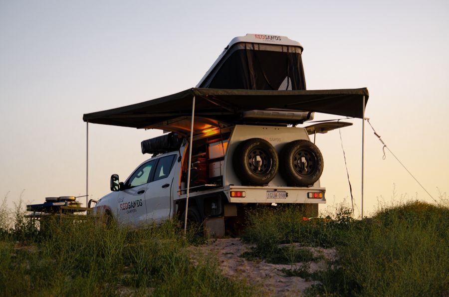 De camper is gereed voor de nacht in een rustieke avondsetting met twee daktenten geopend en de luifel uitgeklapt