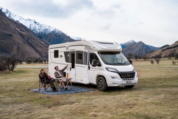 Koppel zit op de campingstoelen aan tafel buiten de Britz Odyssey camper in de bergen van Nieuw-Zeeland