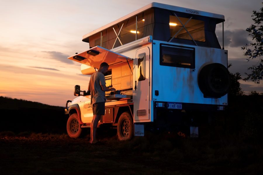De camperreiziger is een maaltijd aan het voorbereiden op het uitschuifbare keukenwerkblad in een prachtige omgeving bij zonsondergang