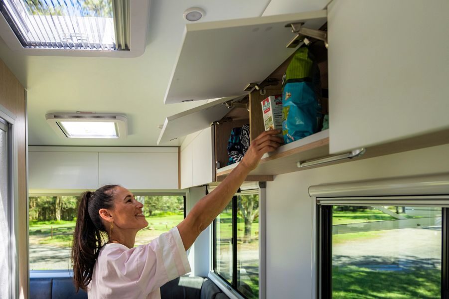 Een vrouw bergt spullen op in de kasten boven de keuken in de Maui Beach camper