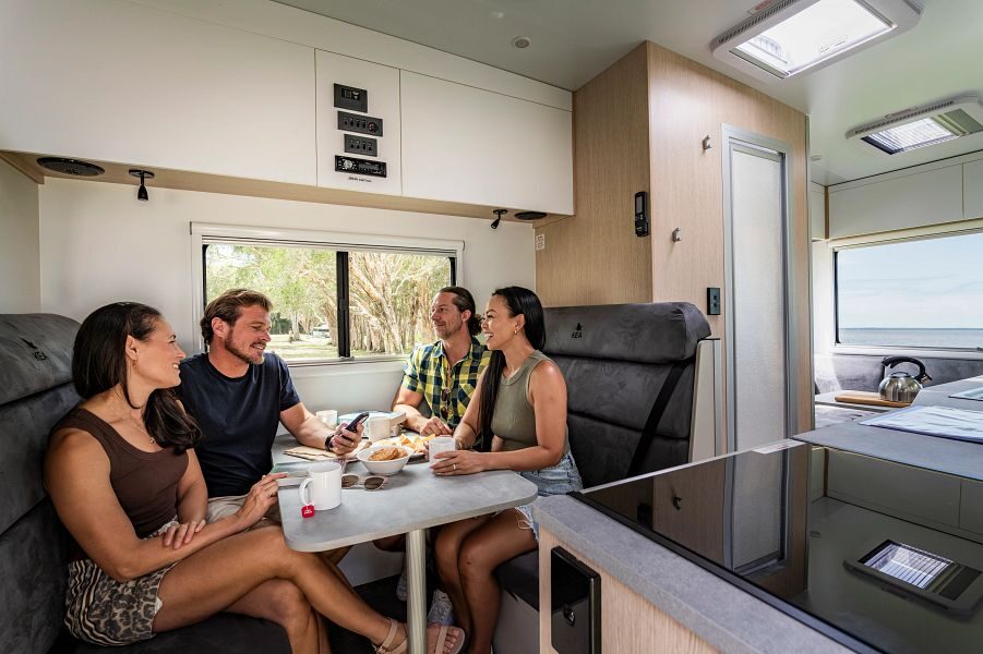 Een vriendengroep zit tegenover elkaar aan tafel in het middelste gedeelte van de Maui Beach camper