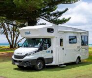 De zijkant en voorkant van de Maui Beach camper die geparkeerd staat naast een boom op een grasveld