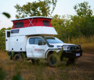 De camper op een gravelweg met zijaanzicht voor een tussenstop, het dak omhoog en de achterdeur geopend