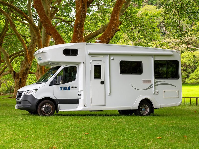 De zijkant van de Maui River camper voor zowel Australië als Nieuw-Zeeland geparkeerd op een grasveld onder een boom