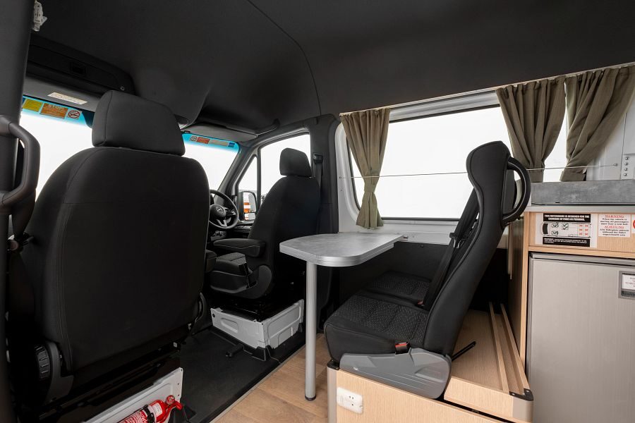 Het interieur van de Mighty Highball camper met de bestuurdersruimte en zitplaatsen met tafel erachter