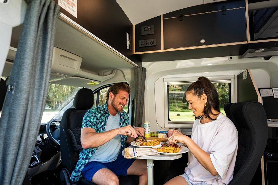 Een koppel is aan het eten terwijl ze in de zithoek van de Mighty Double Down camper zitten met draaibare bestuurdersstoelen