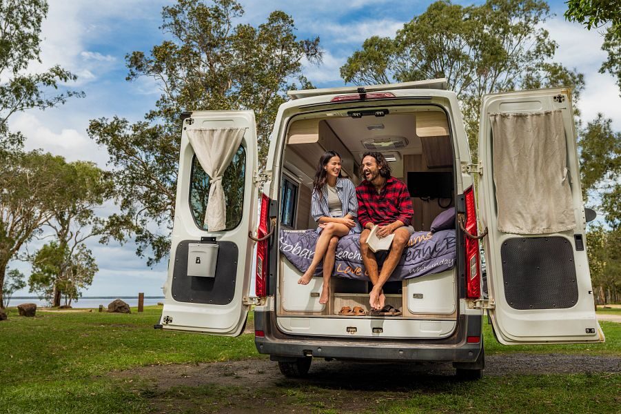 Een koppel zit in de achterkant van de Mighty Duo camper op het tweepersoonsbed met de achterdeuren open