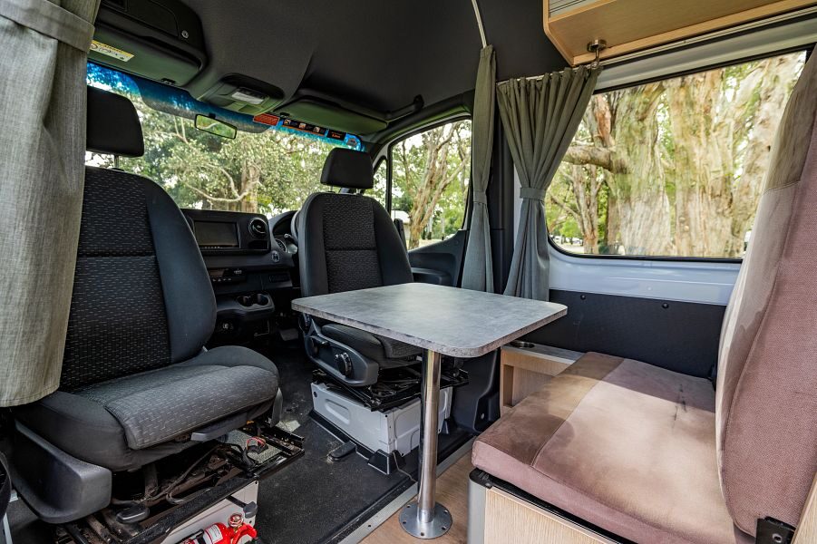 De draaibare stoelen in de cabine gericht naar de achterkant van de camper met tafel en bankje in de Mighty Deuce Plus