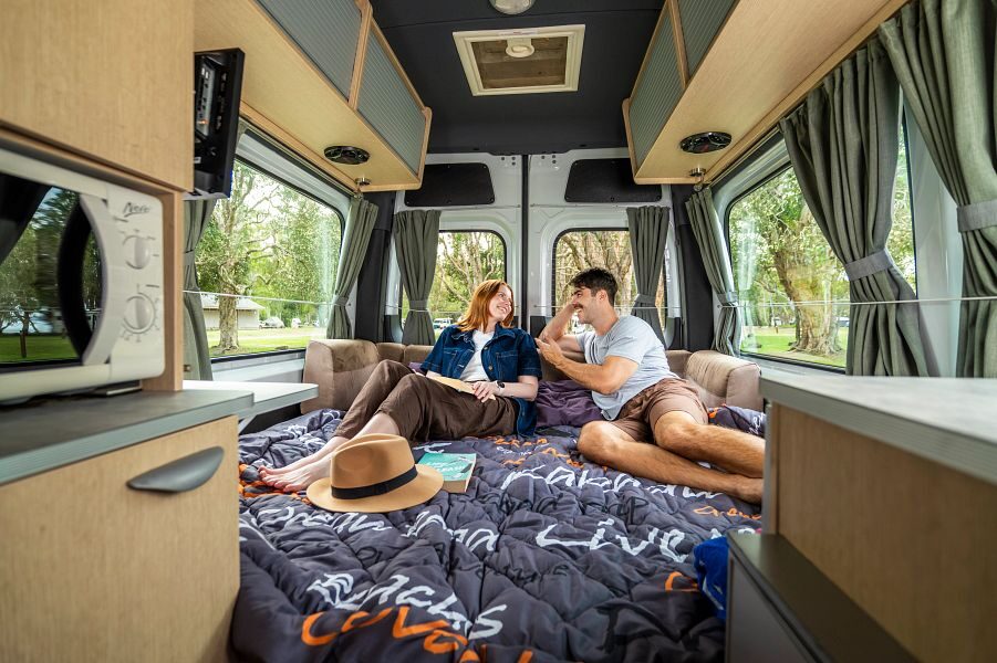 Een koppel kijkt naar elkaar zittend op het tweepersoonsbed in de Mighty Deuce Plus camper