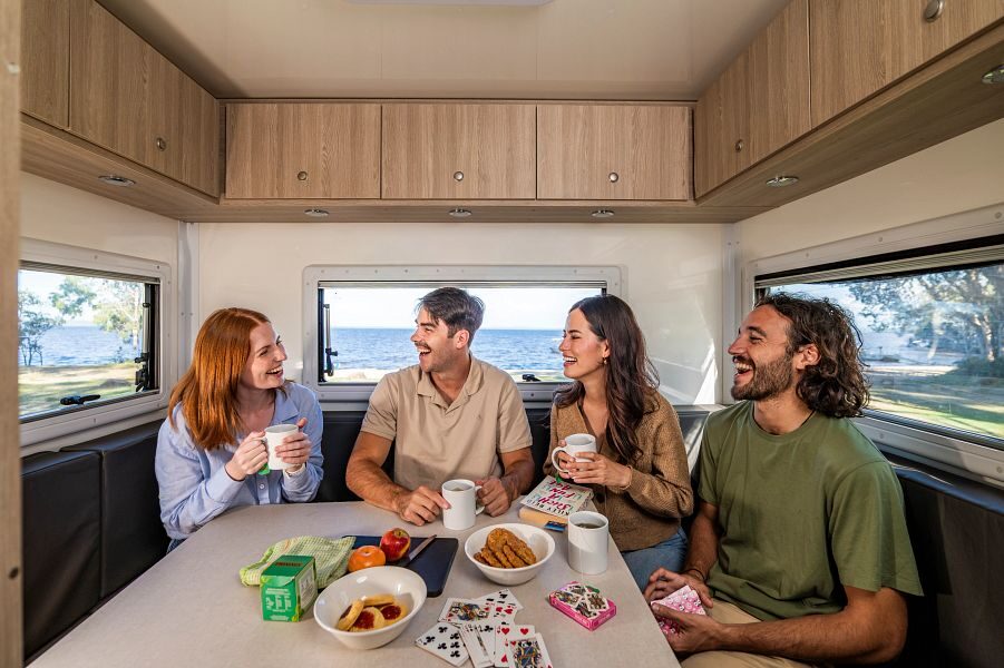 Een vriendengroep speelt een kaartspelletje en zijn samen aan het lachen in de zithoek achterin de Mighty Big Six camper