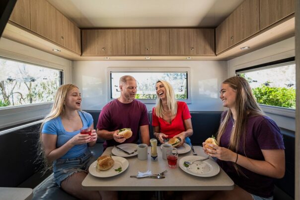 Man en vrouw met twee volwassen dochters zitten in de zithoek van de camper en eten lunch