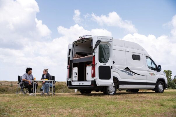 Een stel zit aan de achterkant van de Mighty Lite HiLITE camper op de campingstoelen in de natuur van Nieuw-Zeeland