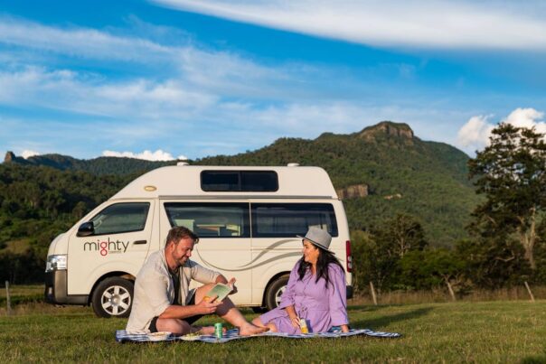 Een stel zit voor de Mighty Lite HiLITE camper op een picknickkleed in het gras in Australië