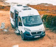 De McRent Urban Plus camper staat in het zand naast de zee met de zijdeur open en het voetstapje uitgeklapt