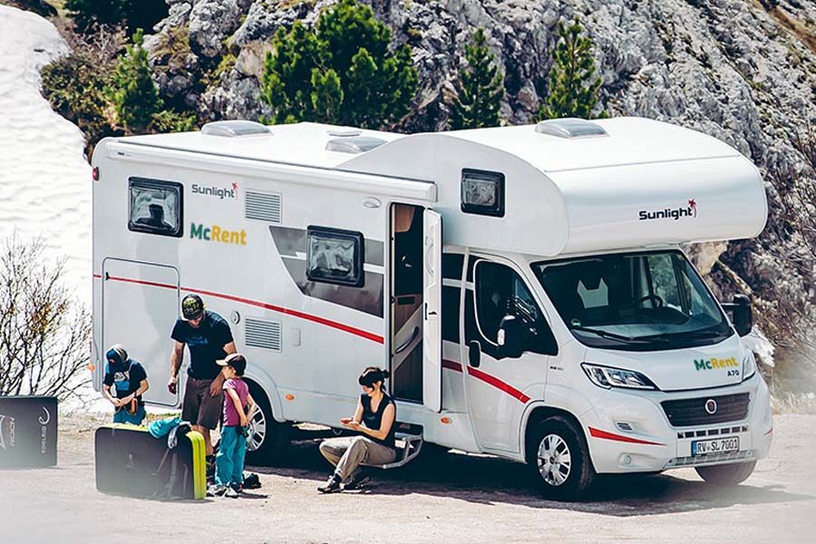 Een man staat met zijn twee kinderen naast de McRent Family Plus camper terwijl zijn vrouw op het opstapje bij de ingang van de camper zit
