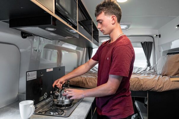 Jongen staat te koken in de Mighty Highball camper in Nieuw-Zeeland
