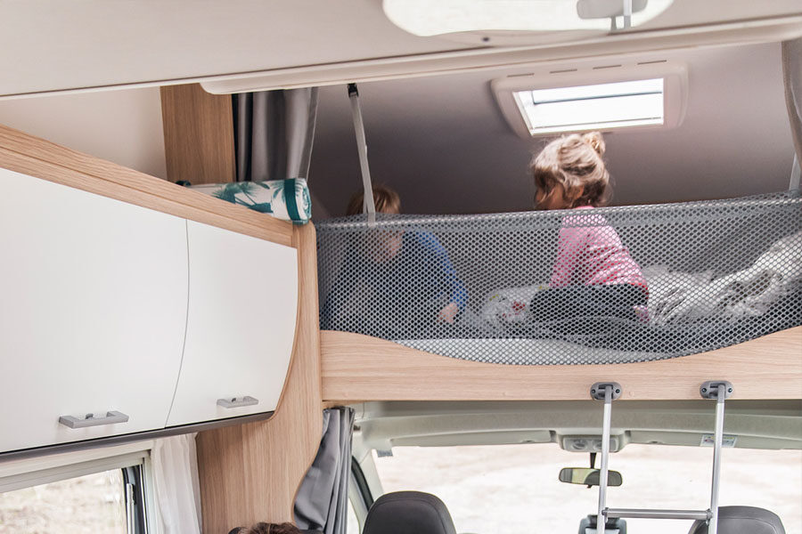 Twee kinderen zitten op het bed in de alkoof met daarvoor een veiligheidsnet in de McRent Family Luxury