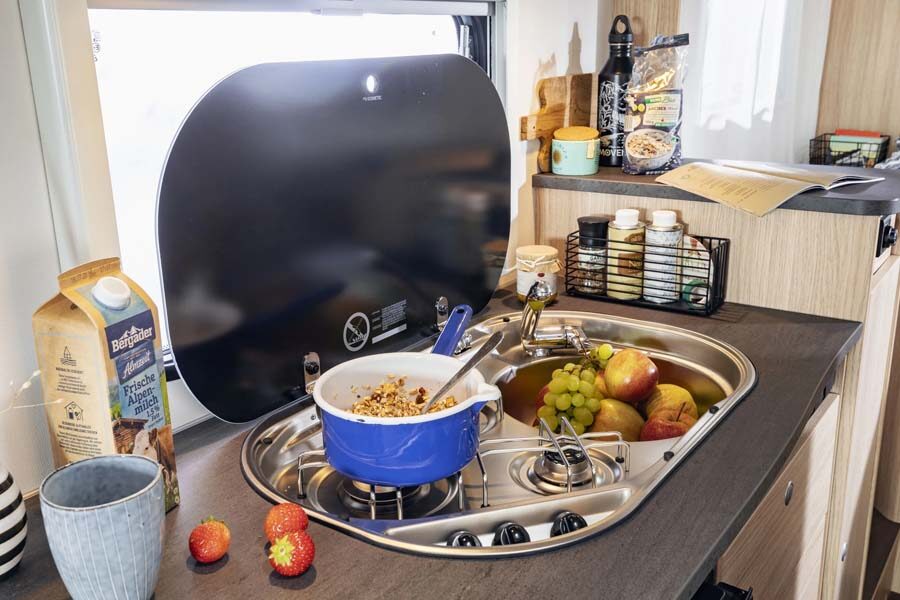 Een pan met eten staat op de gaspit in de keuken van de McRent Compact Plus