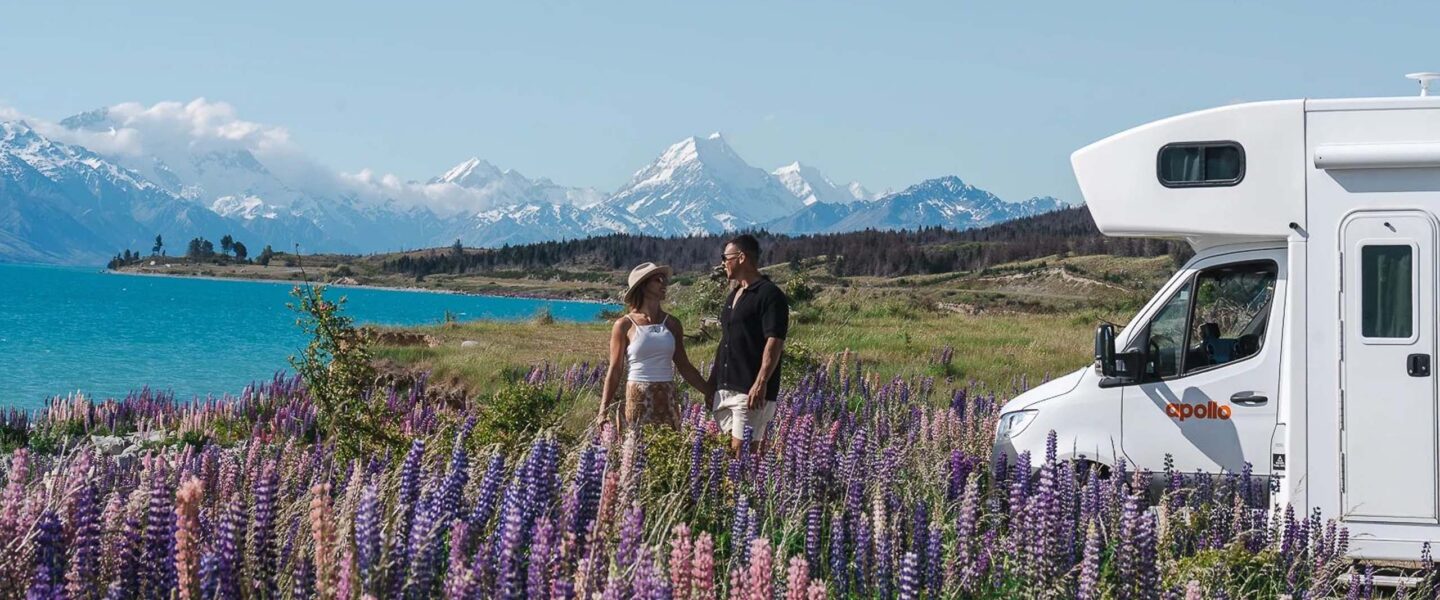 Een koppel staat tussen de lupins naast de Apollo Euro Deluxe camper