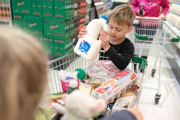 Gezin doet boodschappen, jongen legt fles melk in de kar