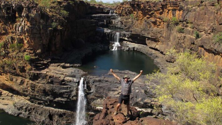 Man staat met zijn armen in de lucht bij de Mitchell Falls