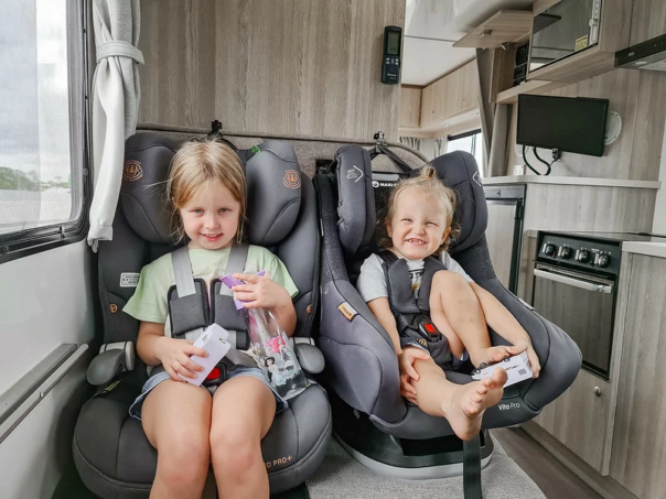 Twee jongere kinderen zitten in kinderautostoelen in de camper