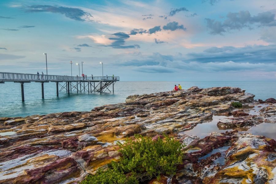 Twee mensen zitten op een rots bij de pier in Darwin naar de zonsondergang te kijken