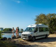 Maui Ultima staat geparkeerd langs het water, mensen staan ernaast